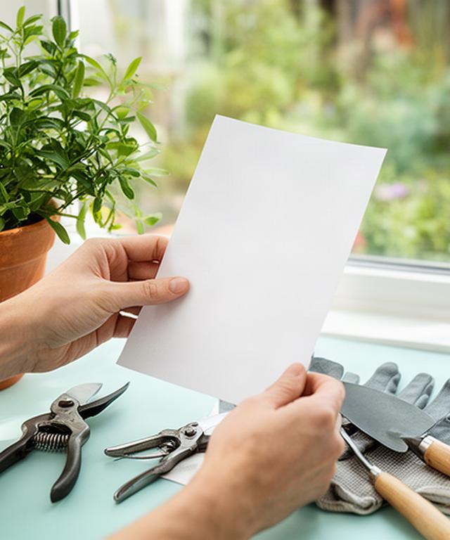 Mani che compilano una richiesta di manutenzione accanto a una pianta in vaso e attrezzi da giardino